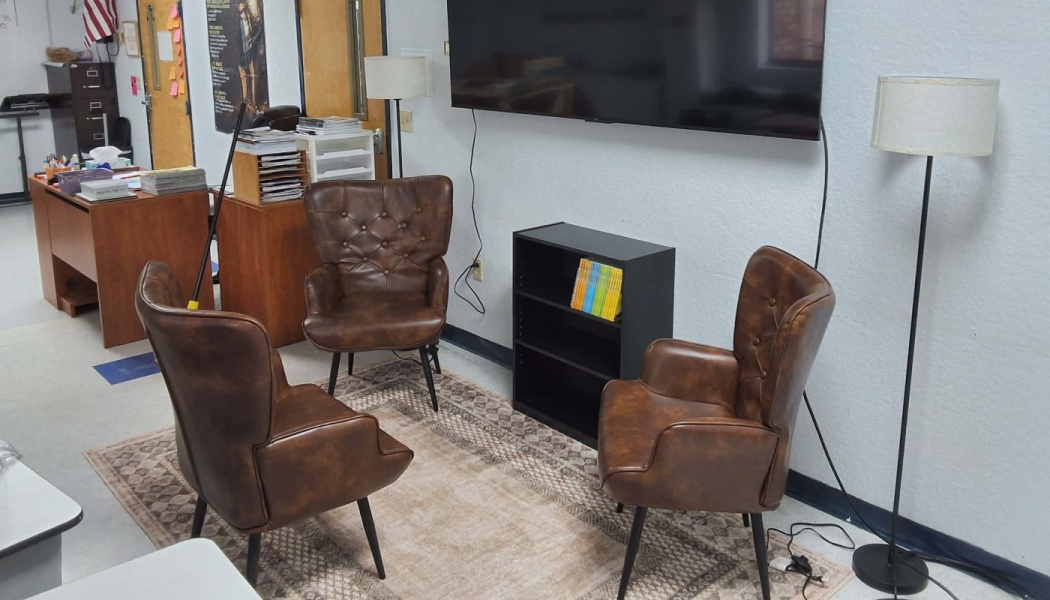 Three brown leather armchairs arranged around a patterned rug in a cozy classroom reading nook with floor lamps.