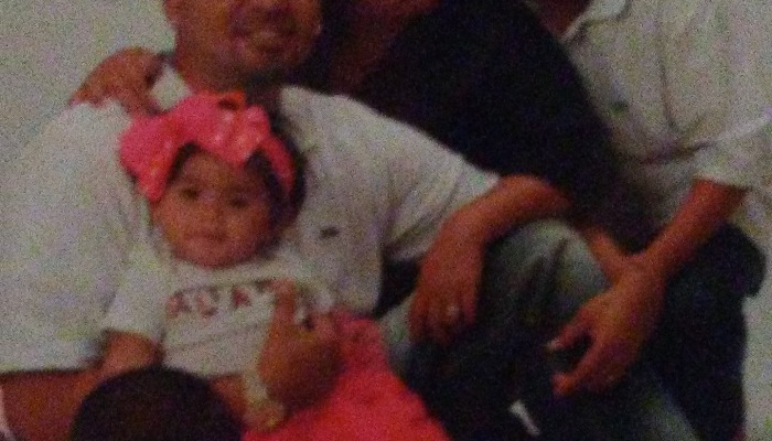 Smiling family portrait featuring a man holding a baby girl with a large bright pink bow headband.