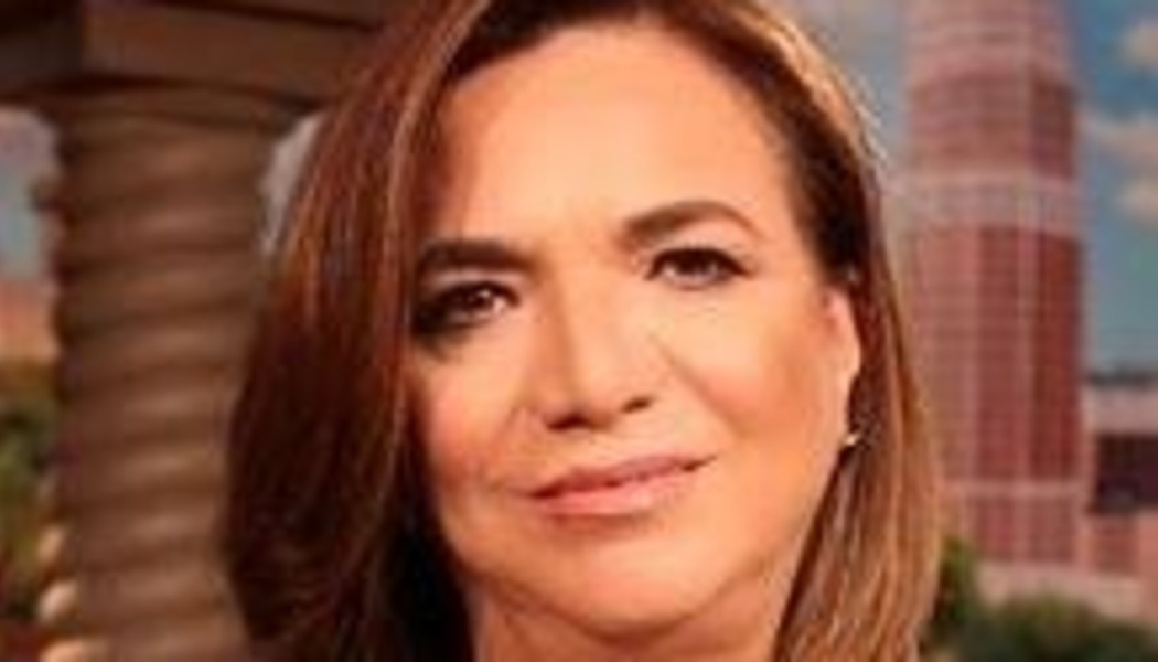 Headshot of a woman with shoulder-length brown hair and a subtle smile against a blurred city background.