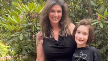 A smiling woman and young child pose together outdoors in front of lush green foliage.