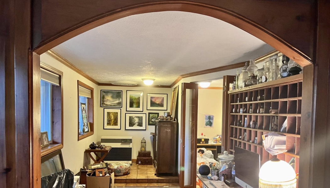 A cozy room with framed artwork and apothecary cubby shelves, viewed through a dark wooden archway.