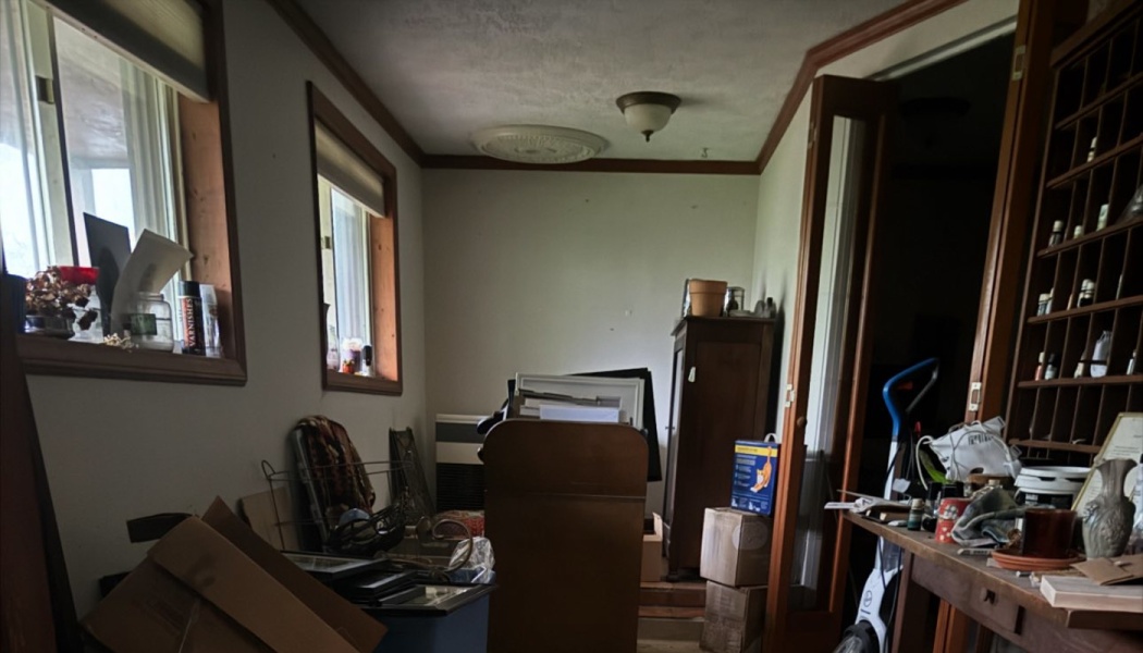 A cluttered room filled with cardboard boxes, furniture, and various household items.