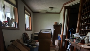 A cluttered room filled with cardboard boxes, furniture, and various household items.