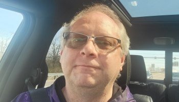 Middle-aged man with glasses and greyish-blonde hair taking a selfie inside a car.
