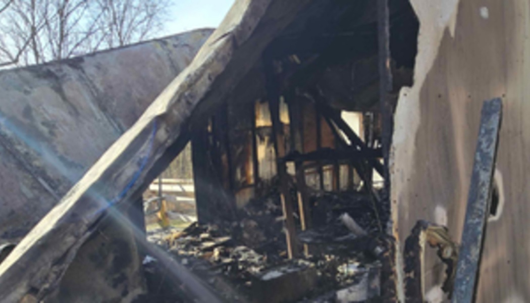 Severely fire-damaged building with a collapsed roof, charred wooden framing, and destroyed interior.