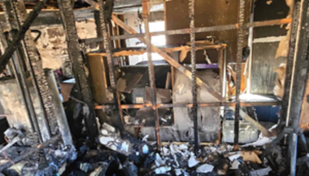 Charred wooden studs and heavy fire damage inside a home surrounded by ash and debris.