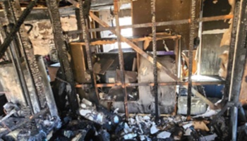 Charred wooden studs and heavy fire damage inside a home surrounded by ash and debris.