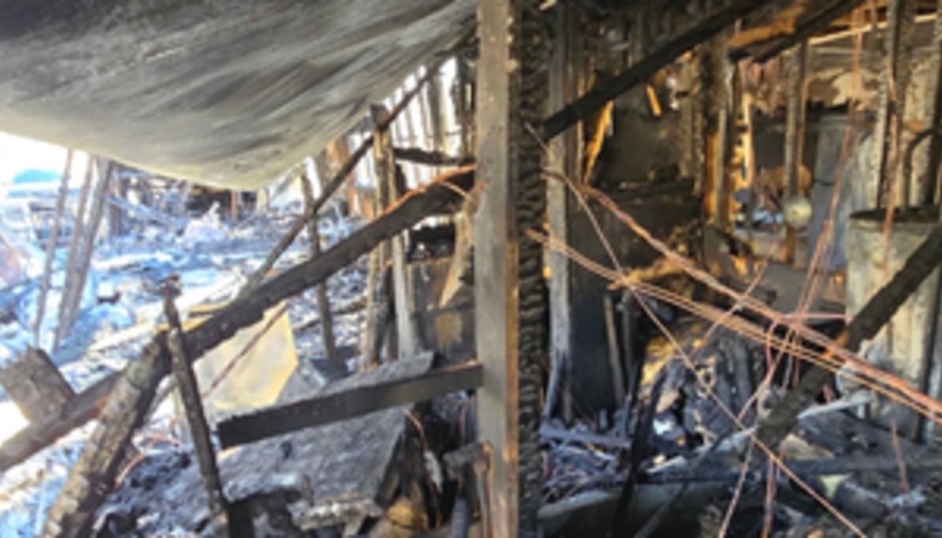 Severely fire-damaged home interior with charred wooden beams, exposed copper wiring, and collapsed structural debris.