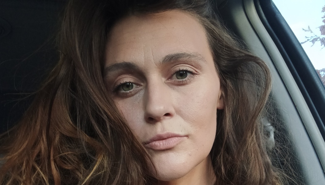 Close-up portrait of a woman with long wavy brown hair and green eyes looking directly at the camera.
