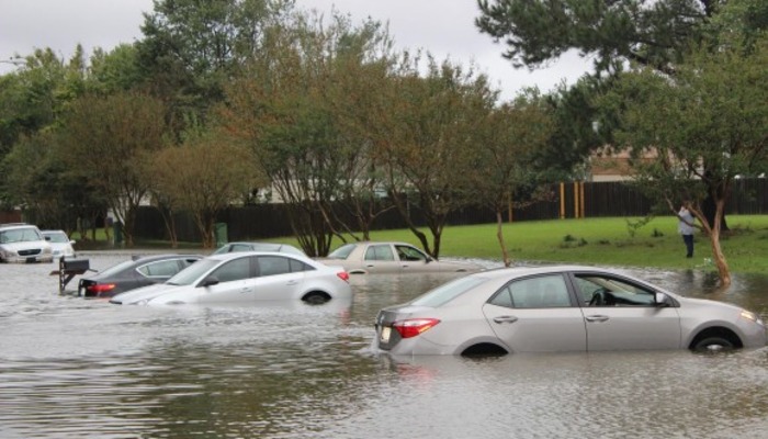 Several cars partially submerged in deep floodwaters on a suburban residential street.