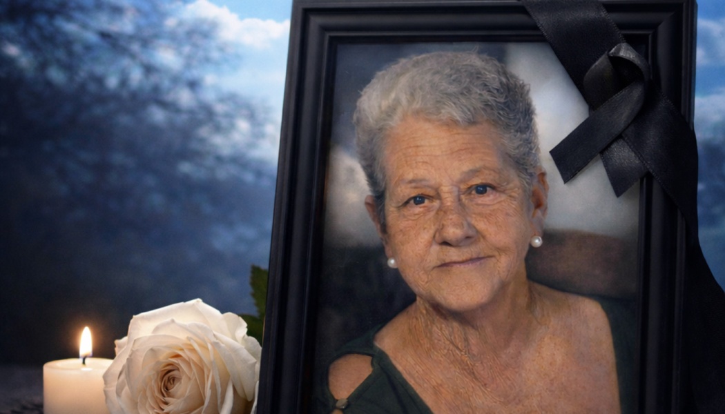 Framed portrait of an elderly woman with a black ribbon, next to a lit white candle and a white rose.