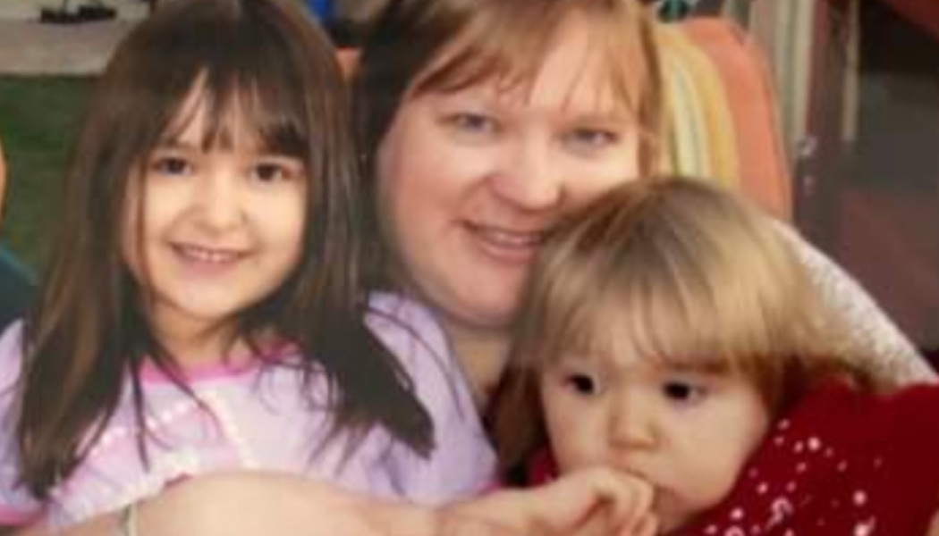 A smiling mother poses closely with her two young daughters.