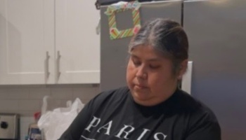A woman wearing a black Paris t-shirt looking down thoughtfully in her kitchen.