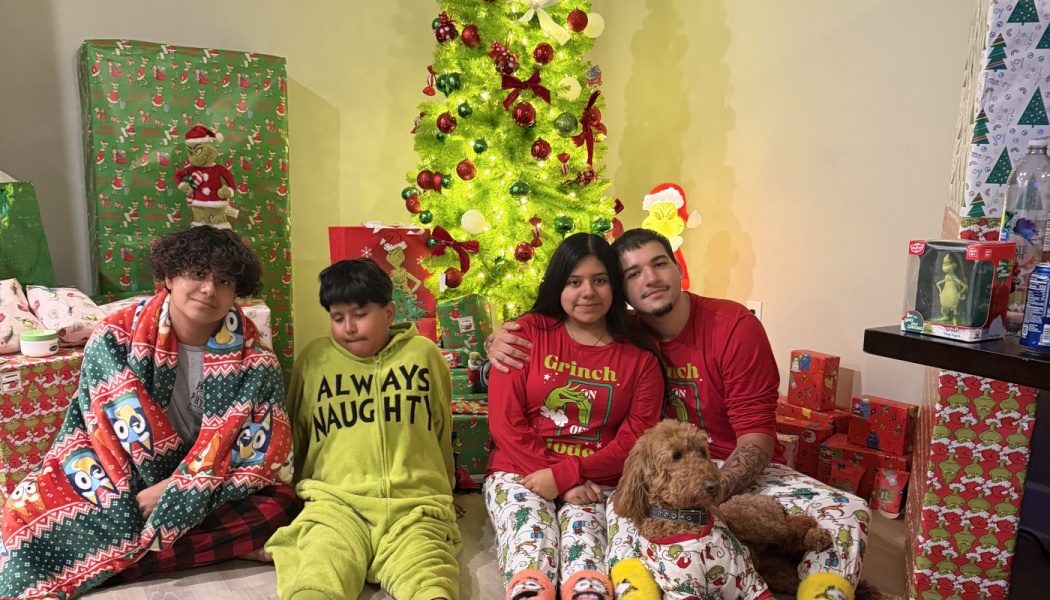 Four family members and a dog pose in festive holiday pajamas in front of a decorated Christmas tree with presents.