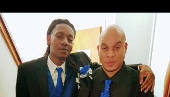 Two men dressed in formal suits with matching blue ties pose together with arms around each other.