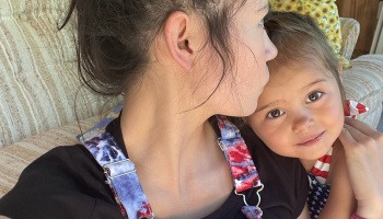 A young girl smiling at the camera while leaning affectionately against her mother.