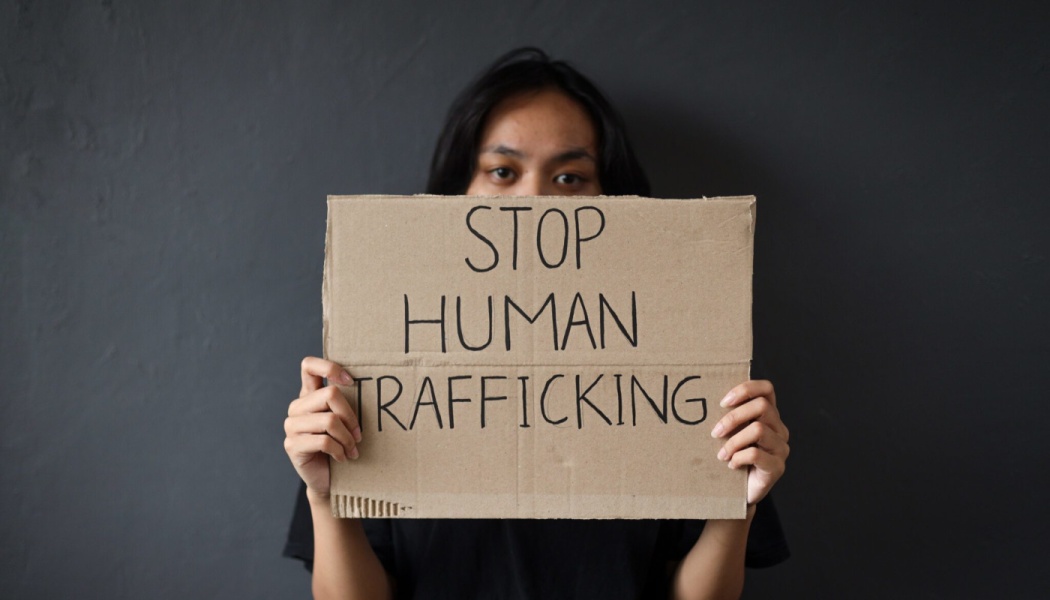 A person holding a cardboard sign reading "STOP HUMAN TRAFFICKING" in front of their face.