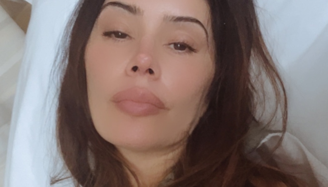 Close-up of a dark-haired woman lying on a white pillow, looking into the camera.