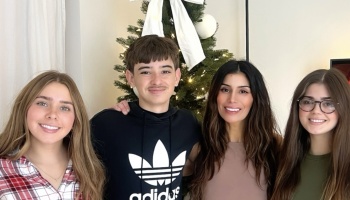 A smiling mother and her three children pose together in front of a decorated Christmas tree.