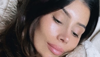 Close-up of a woman with dark hair resting her head on a pillow with a gentle expression.