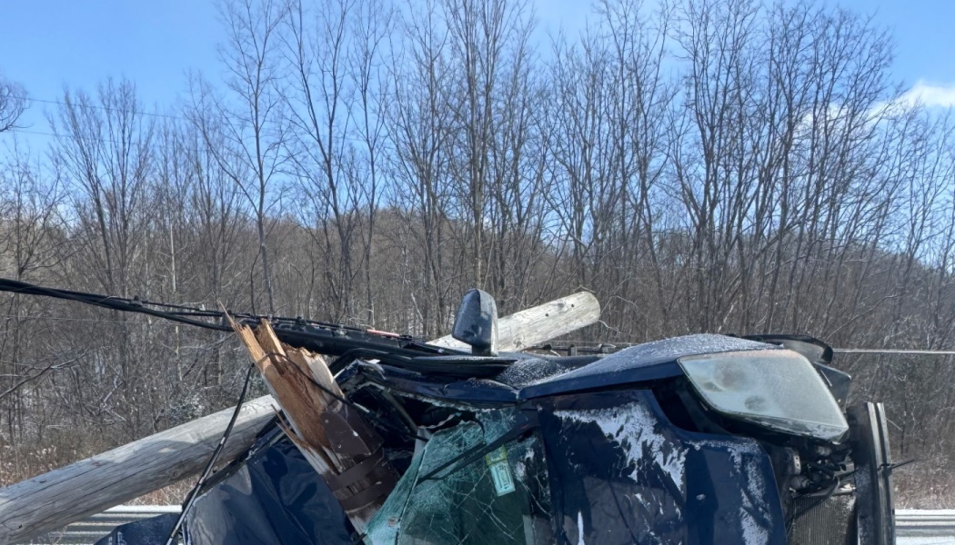 A severely crushed blue car with a broken wooden utility pole resting across its crumpled roof.