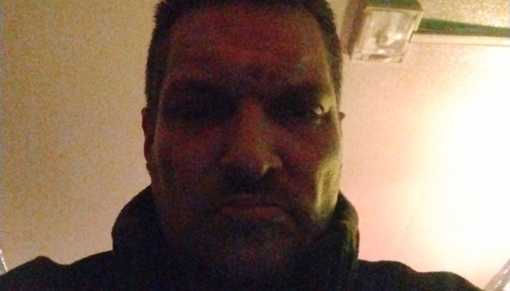 Close-up selfie of a man with a serious expression in dim lighting, shot from a low angle.
