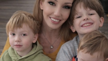 A smiling blonde woman posing closely with her three young, happy children.