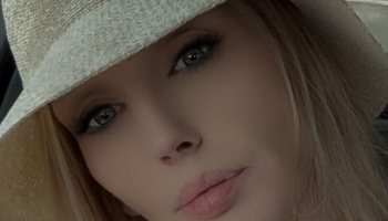 Close-up portrait of a blonde woman with blue eyes wearing a woven straw hat.