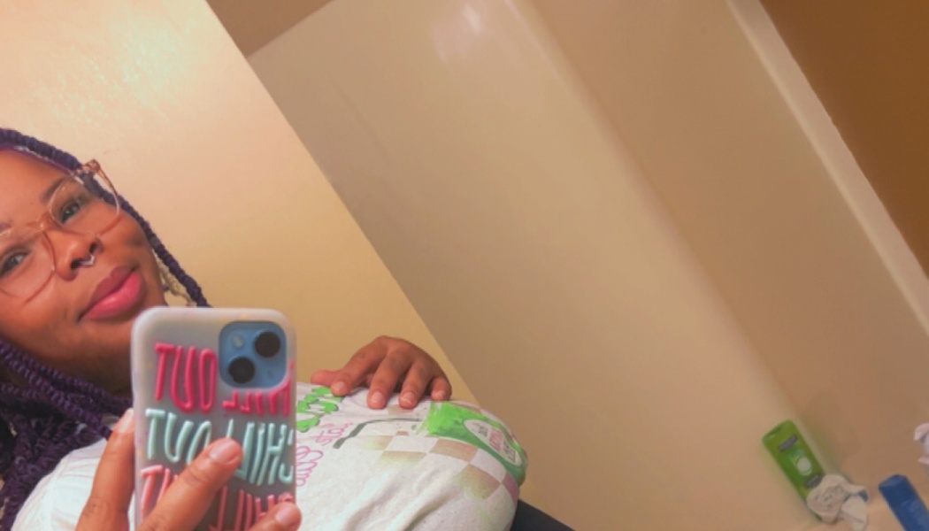 A smiling woman with purple braided hair and glasses taking a mirror selfie.