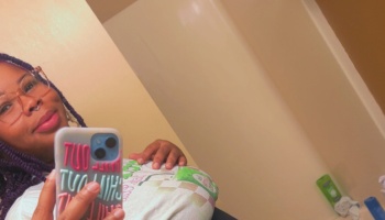 A smiling woman with purple braided hair and glasses taking a mirror selfie.