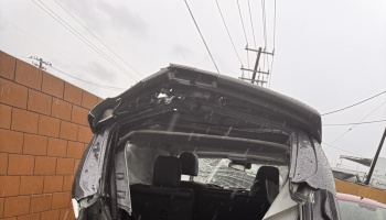 Severely crushed roof and frame of a dark vehicle in falling rain with deployed airbags visible inside.