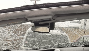 Severely shattered car windshield with spiderweb cracks and raindrops, viewed from inside the vehicle.