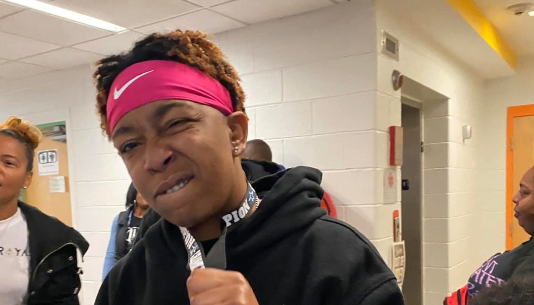 Young person wearing a pink Nike headband and black hoodie, making a confident, playful face in a hallway.