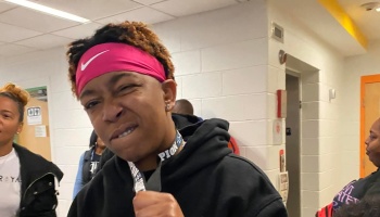 Young person wearing a pink Nike headband and black hoodie, making a confident, playful face in a hallway.