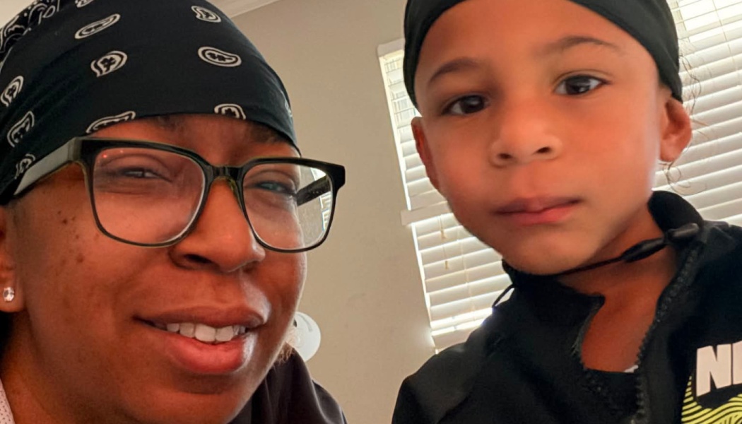 Close-up selfie of a smiling woman in glasses and a black headwrap posing beside a young boy.