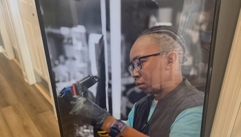 A focused technician with glasses and gloves carefully working on a mechanical component in a workshop.