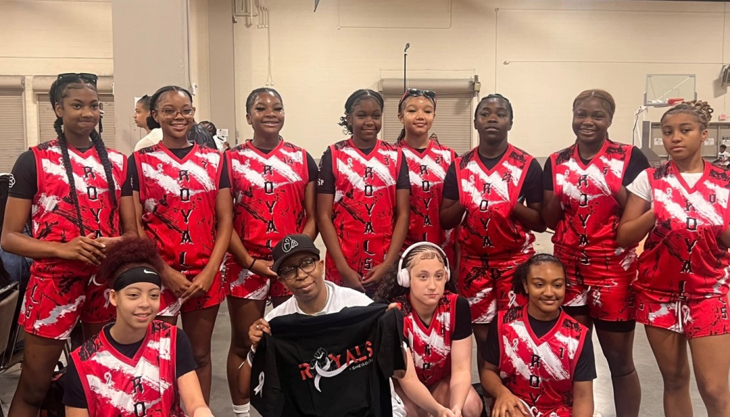 A youth girls' basketball team in matching red and white Royals jerseys poses together with their coach.