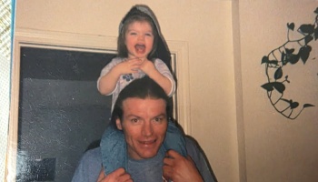 A smiling man giving a laughing young child a ride on his shoulders.
