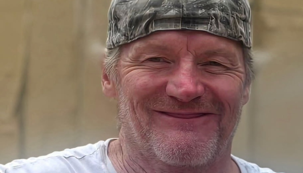 Close-up portrait of a smiling middle-aged man wearing a camouflage cap and white t-shirt.