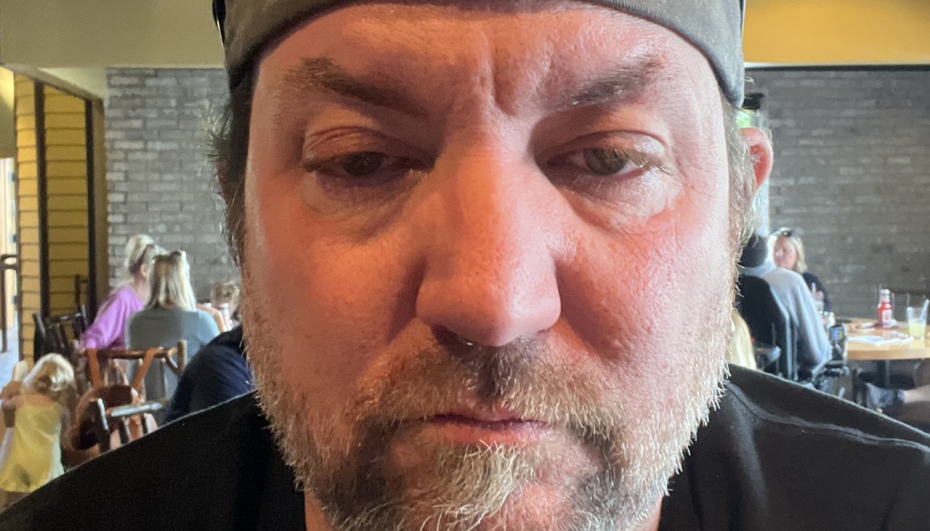 Close-up selfie of a man with a grey cap and light beard looking at the camera inside a restaurant.