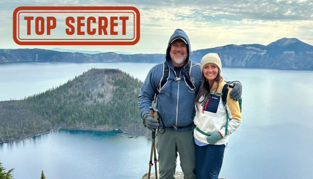 A smiling couple poses above a crater lake with a red TOP SECRET stamp graphic in the top left.