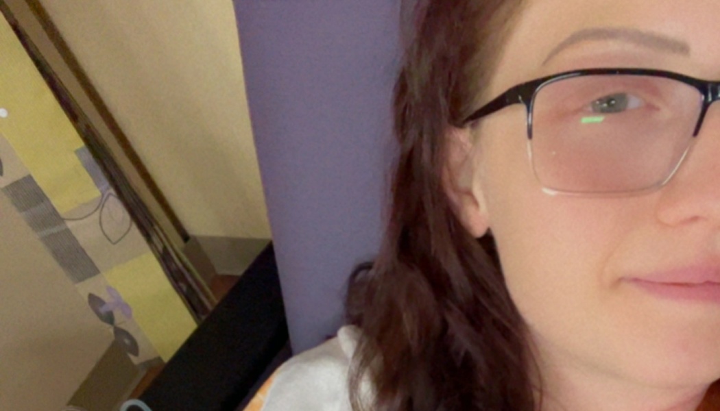 Close-up selfie of a woman with dark hair and glasses resting against a purple cushion.