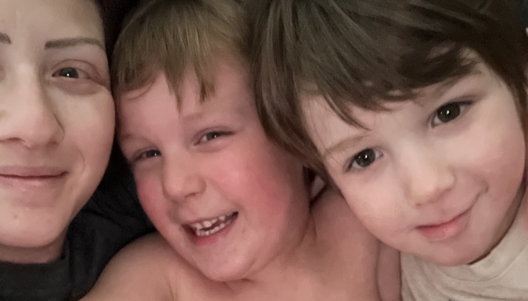 A smiling mother lying close together with her two young sons.