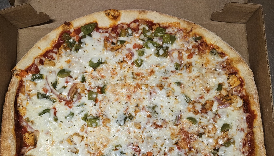 Freshly baked pizza with melted cheese, green peppers, chicken, and red onion inside an open cardboard box.