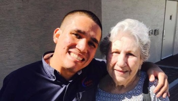 A smiling young man puts his arm around a smiling elderly woman.
