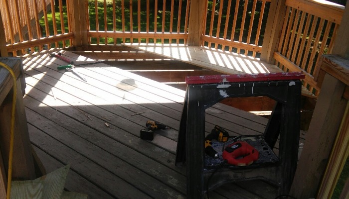 Power tools rest on a sawhorse and wooden deck during a deck construction and repair project.