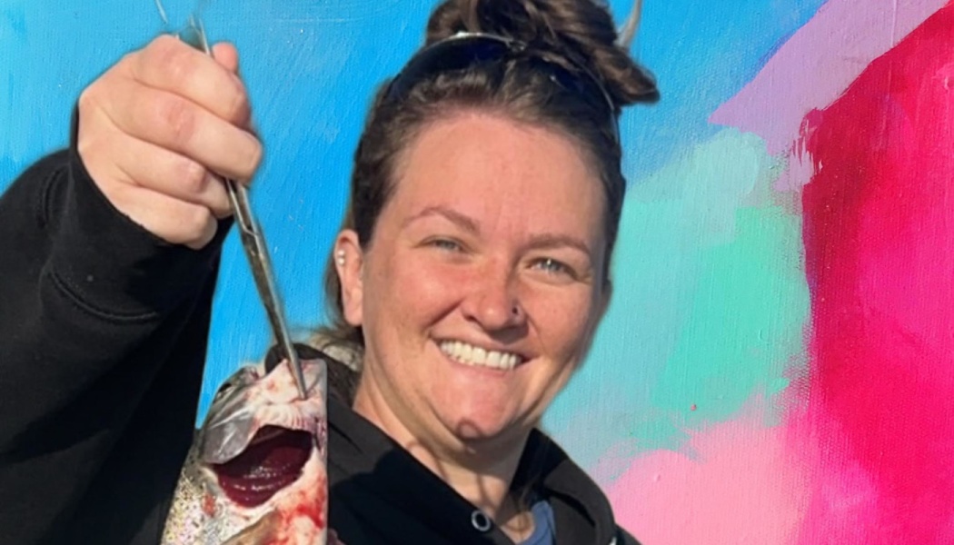 Smiling woman holding up a caught fish with pliers against a bright, colorful painted background.