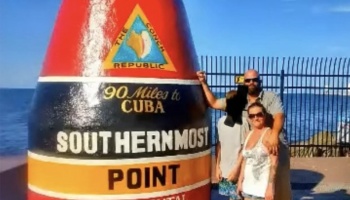 A family poses beside the colorful Southernmost Point buoy monument in Key West, Florida.