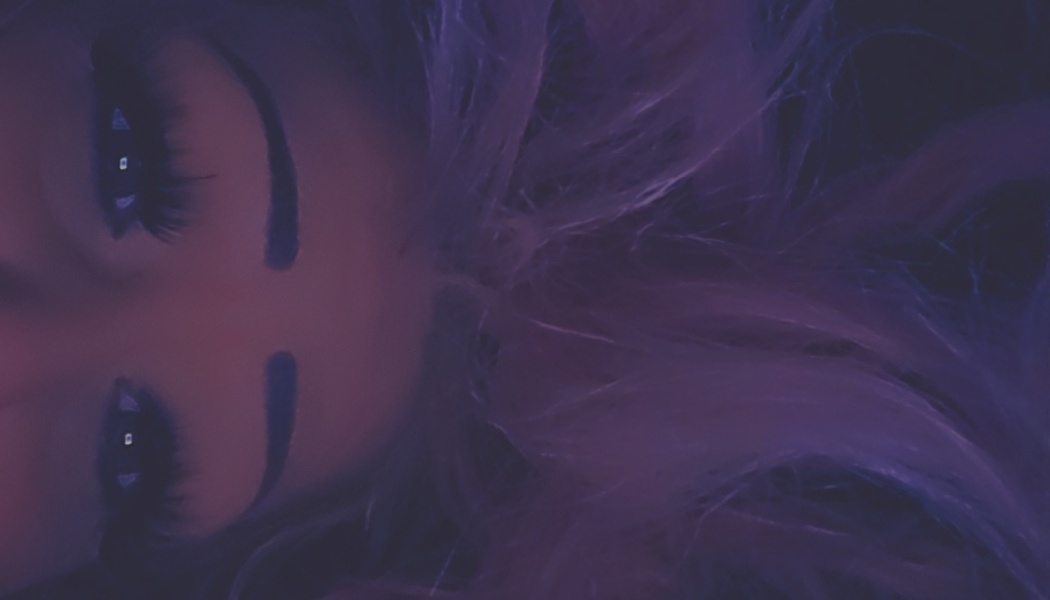 Close-up portrait of a person with dramatic eye makeup and flowing purple hair under dim neon lighting.