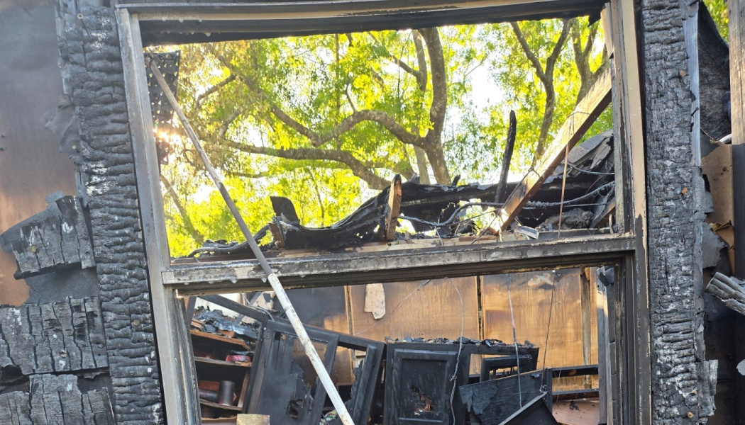Charred wooden window frame revealing the burnt, collapsed interior of a home destroyed by fire.